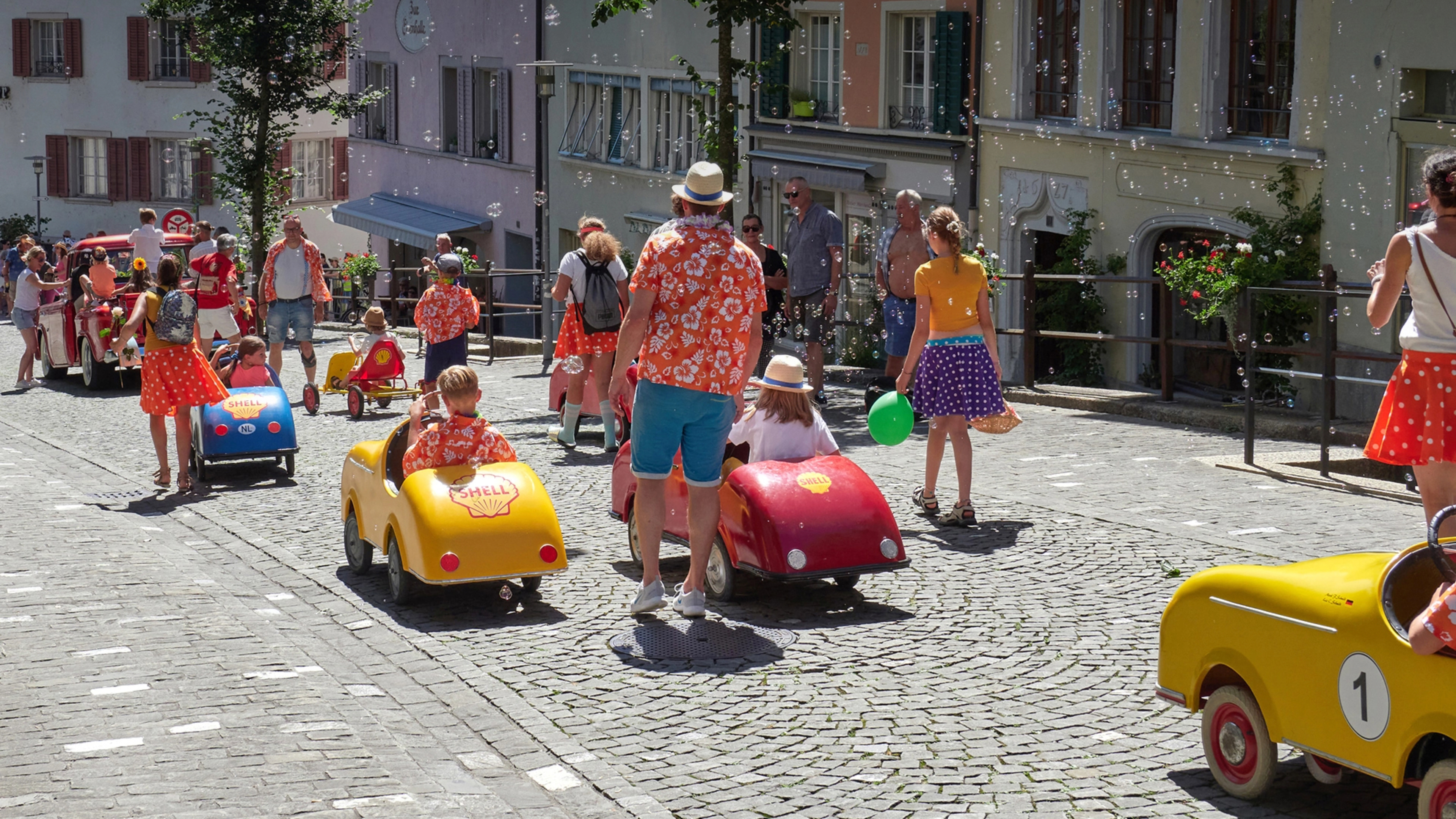 Tretauto Hero Bild, Altstadt Bremgarten im Sommer, mehrere Kinder mit Ihren Tretautos fahren hinunter zum Reuss, von Erwachsenen begleitet